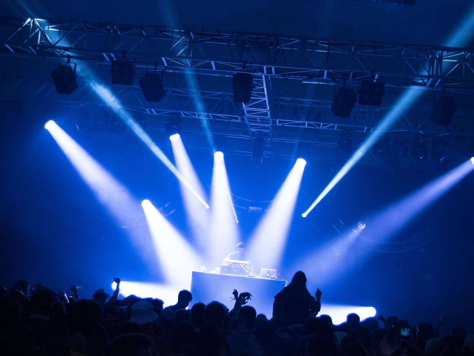 Blue and white stage light beams over a live event crowd, seen from behind