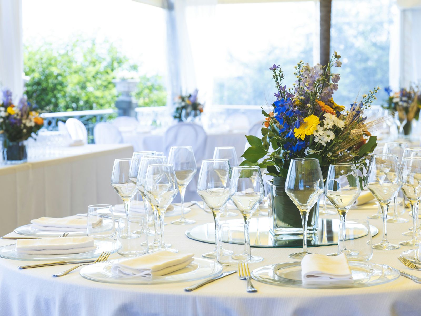 Round banquet table with white linen, glassware and a wildflower centrepiece in a sunlit marquee