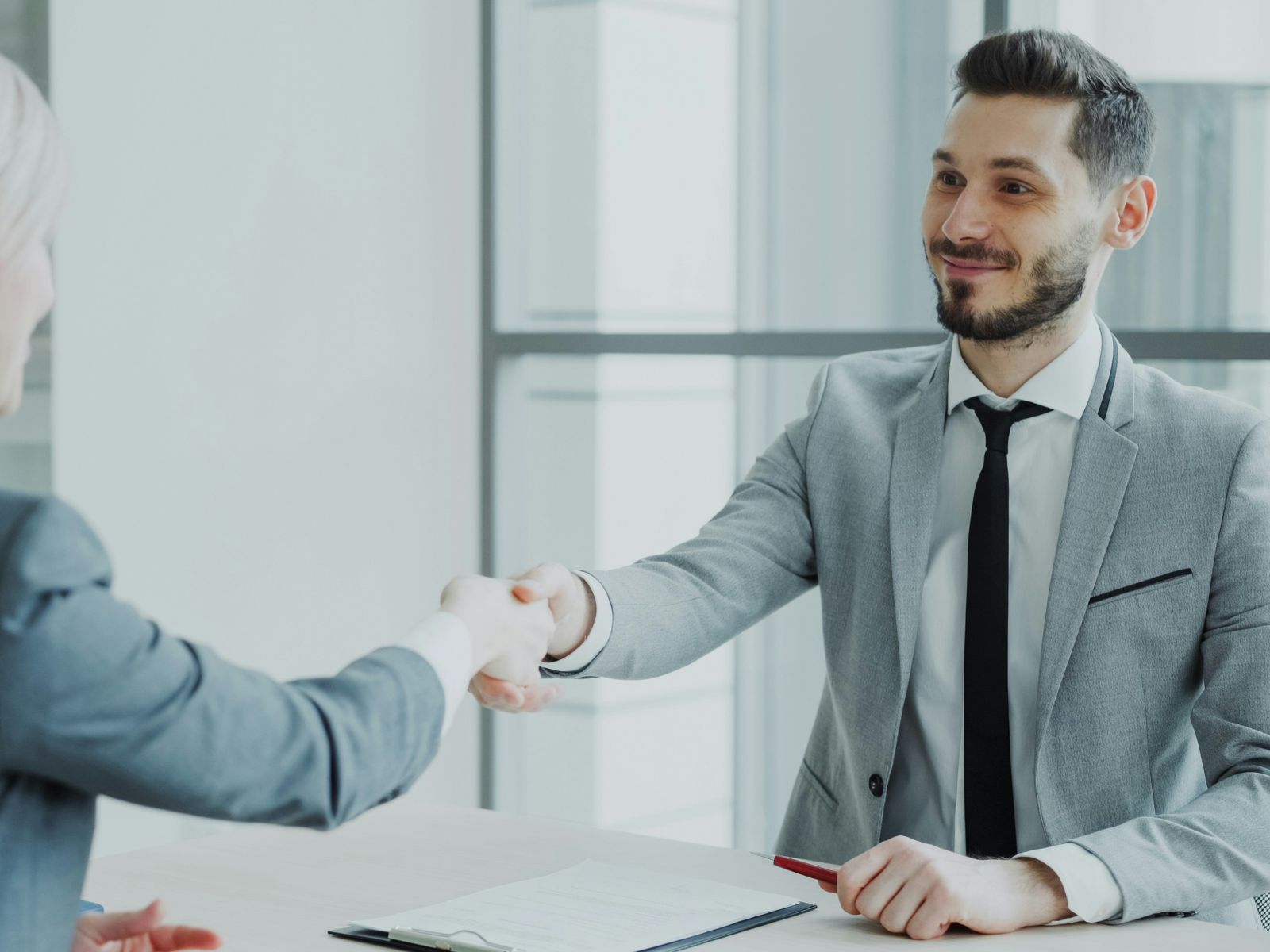 Two professionals shaking hands across a desk in a bright white office