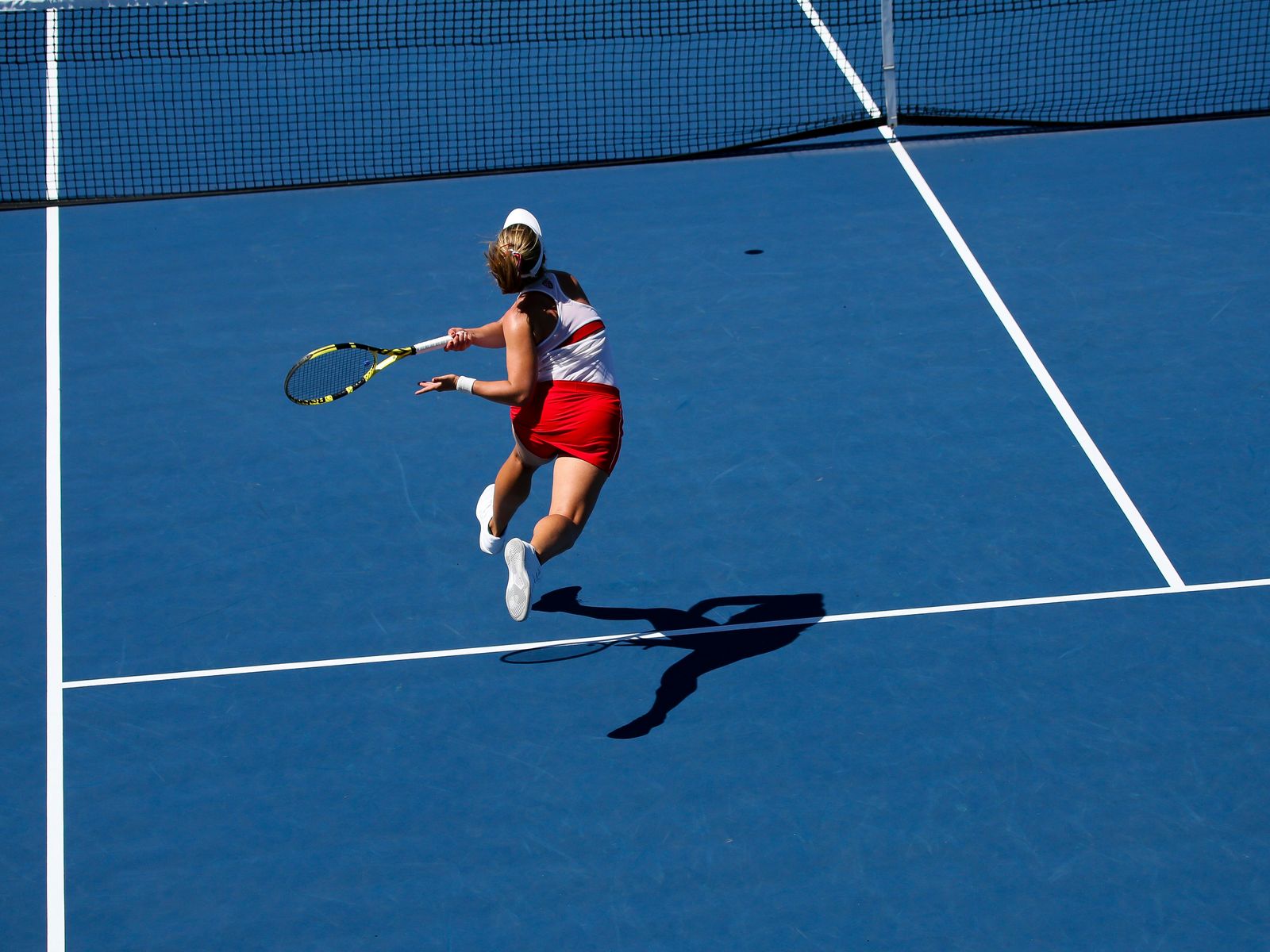 Tennis player hitting a forehand on a blue hard court, seen from above